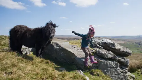 Getty Images Young girl jumps from rocks near horse