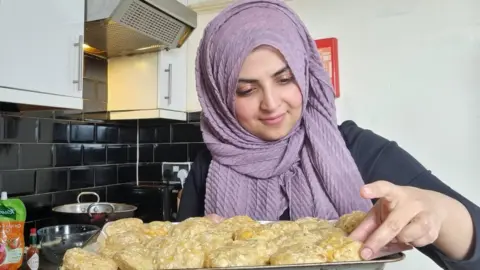 Saima Salahhuddin Chef Saima holds up tray of baked goods in her kitchen