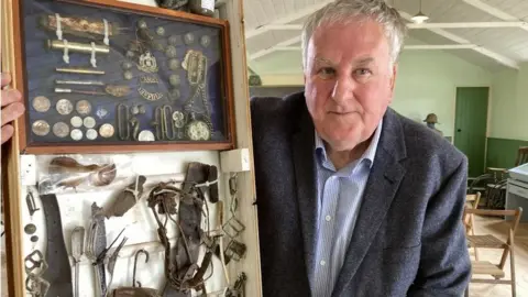 Martin Giles/BBC Colin Fakes holds a display case of L/Sgt Charles Steven's possessions, found with his body when it was discovered in France