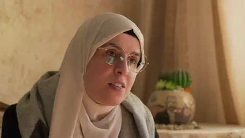 BBC Palestinian journalist Bushra al-Taweel wearing a cream headscarf and glasses in her family apartment in Ramallah