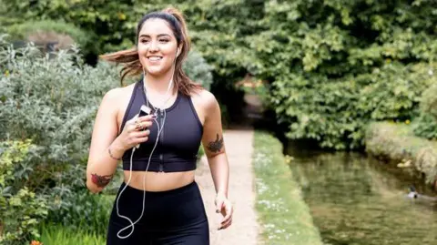 A woman is running and listening to earphones while following a path through a park.