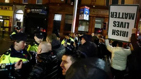 Reuters Police officers form a line as a crowd of people gather in Dublin city centre, with one man holding a sign that reads: IRISH LIVES MATTER