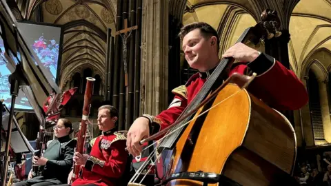 BBC People sitting down in Grenadier Guards Band uniform playing instruments