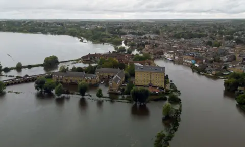 PA Media A bird's eye view of a river surrounded by flood water with houses in the middle