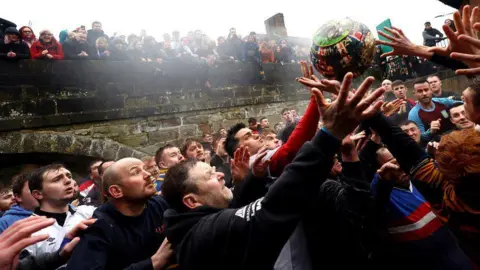 Reuters Huge crowds take part in the game. Several men stretch for the ball as spectators watch on from behind 