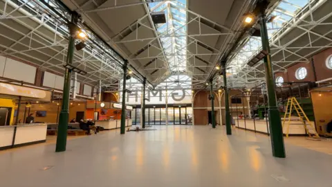 Bright, newly refurbished Goole Market Hall with a high glass roof, exposed dark green beams, and open floor space. Modern food‑stall units line the edges.