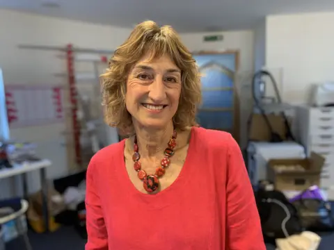 A lady with a red top and brown hair smiles at the camera.