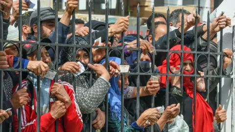 AFP People holding their ID cards outside a government building in Mnihla, Tunisia - Monday 30 March 2020