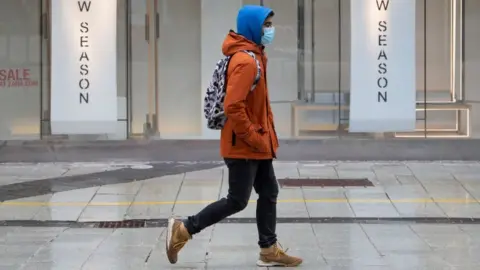 Getty Images Man walking in front of closed shop.