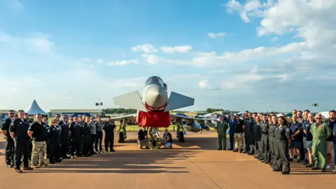 RAF/BBMF A wreath to Mark Long in front of a Typhoon modern-day fighter, flanked by hoards of RAF service personnel and a  wreath was laid at the Royal International Air Tattoo