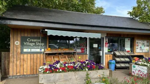 James Grant/BBC Small single-storey wooden shop building with flowers outside