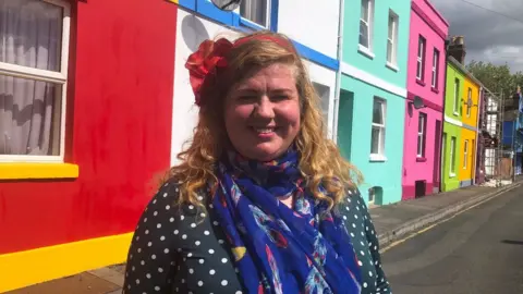 BBC Tash Frootko founder of the Rainbow House project stood in front of colourful houses