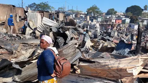 Woman in front of burnt shacks