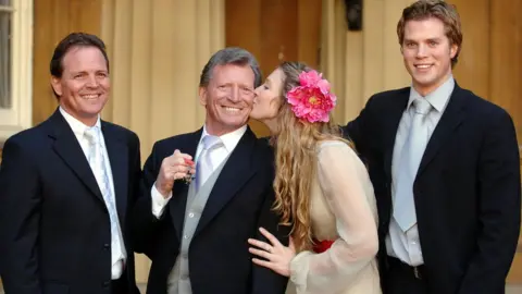 PA Media Johnny Briggs, with children (left to right) Mark, Stephanie, and Michael after collecting an MBE from the Queen at Buckingham Palace