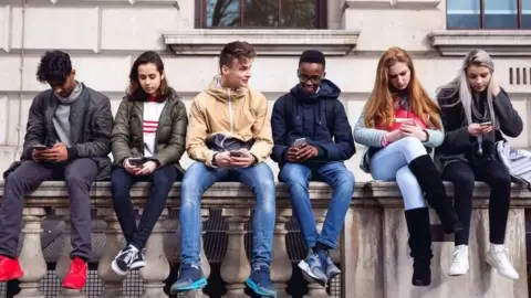 Getty Images Young people sat on a wall on mobile phones