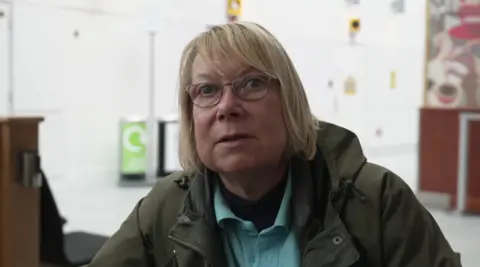 A woman with short blonde hair and glasses inside an airport