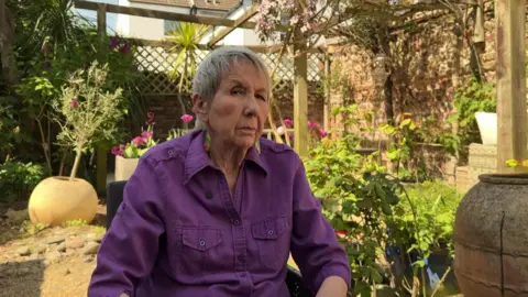 George Carden/BBC Sylvia Holder say in a garden looking to camera. She is wearing a purple top.