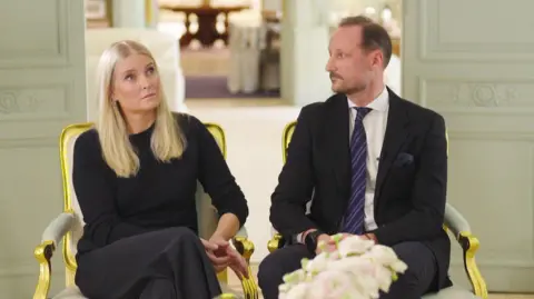 NRK A woman with blonde hair sits next to a man in a suit