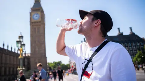 PA Media A man in a white t-shirt and black cap cools down with a bottle of water during the hot weather in Westminster Bridge, central London. 