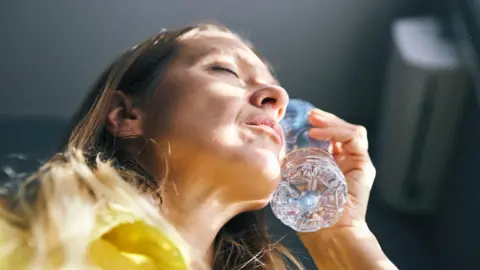 Getty Images A woman holding a bottle of water to her face in a bid to cool herself