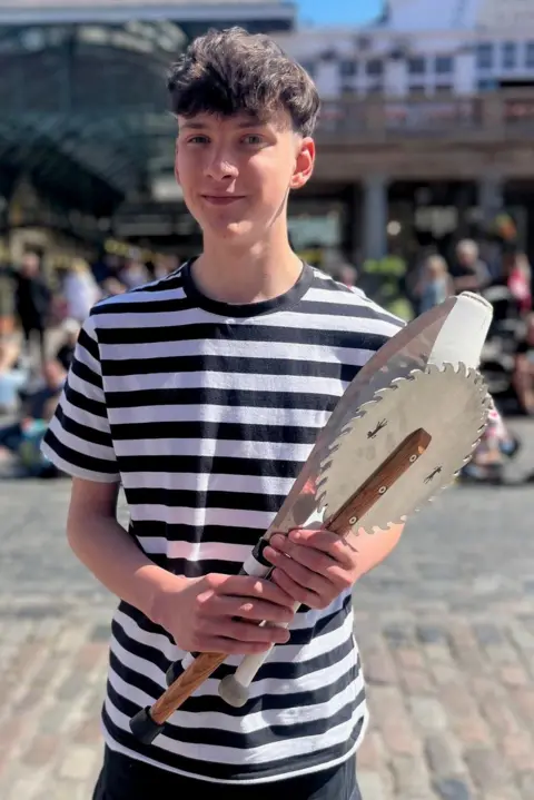 A 16-year-old boy wearing a stripy T-shirt and holding serrated juggling clubs.