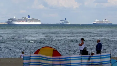 PA Media People on the beach at Studland look out at the cruise ships