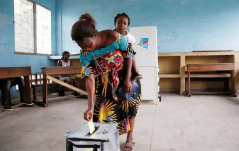 Reuters Woman casting her vote with a baby on her back.