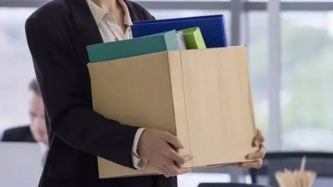 Getty Images A woman carries a box after losing her job