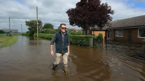 Danny Lawson/PA Wire Man walking down a flooded road in Wainfleet