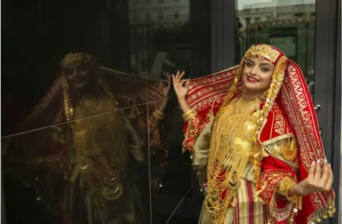 Getty Images Woman smiling in a gold and red traditional Tunisian outfit.
