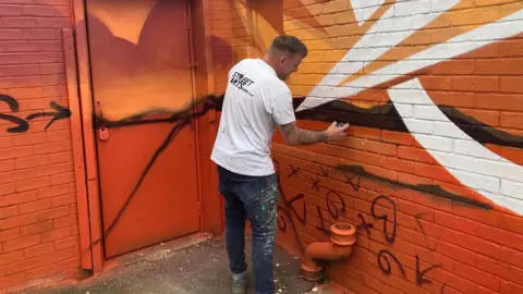 Nadia Gyane/BBC Nathan painting an old toilet block