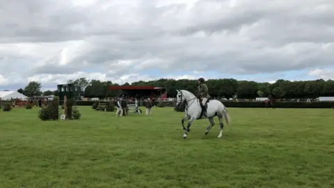 A white horse being ridden. There are multiple fences.