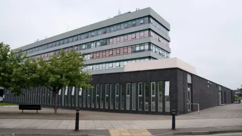 BBC The exterior of Shrewsbury Crown Court, a large, four-storey building with lots of windows. There is a bench, a couple of small trees and a large paved area at the front.
