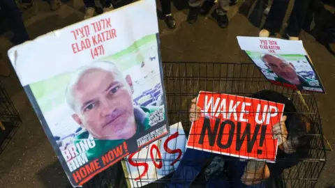 AFP A man sits in a cage with portraits of hostage Elad Katzir during a demonstration in Tel Aviv in March