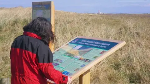 IOM GOV Visitor reading visitor information board at Ayres National Nature Reserve