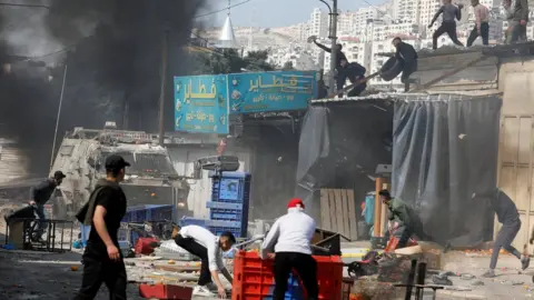 Reuters Palestinians throw objects at Israeli forces during a raid in Nablus, in the occupied West Bank, on 22 February 2023