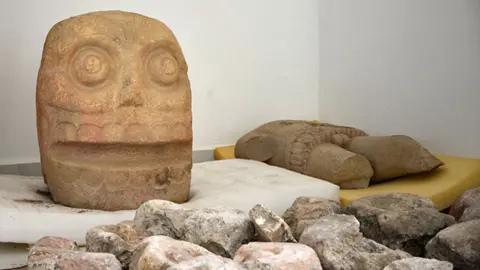 Melitón Tapia INAH A large stone head and a torso of the God pictured on display