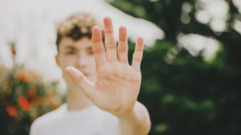 Getty Images Young man holds up hand in "stop" motion