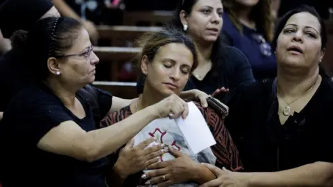 Reuters The wife of Coptic priest Abdul Masih Bakhit holds part of his vestments at a funeral service at the Church of the Blessed Virgin Mary in Giza, Egypt (14 August 2022)