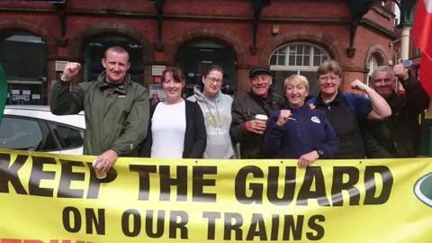 Pat Draper People waving banners at a picket line in front of a train station