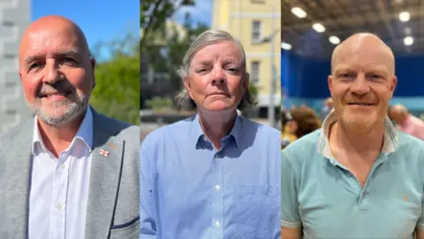 From left to right, Jonathan Le Tocq a man who is bald with a grey beard, wearing a grey suit and a Guernsey lapel pin, with a white shirt. 

In the middle, Deputy Charles Parkinson who has shoulder length grey hair, and a blue checked shirt.

On the right Deputy Gavin St Pier, a bald man with a ginger beard and a pale blue shirt. 