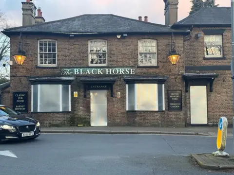 Black Horse Black Horse pub sign on yellow brick building with metal shutters over door and window