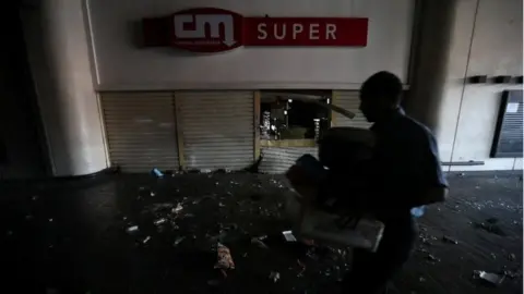 Reuters A shop employee helps clean up the area after the shop was looted during an ongoing blackout in Caracas, Venezuela, March 10, 2019.