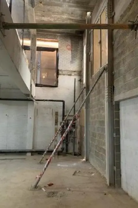 HSE A large, unfinished space with concrete walls and a high ceiling. A doorway cavity can be seen boarded up.