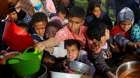 Reuters Palestinian children gather to receive food cooked by a charity kitchen, during the Muslim holy month of Ramadan, in Khan Younis, in the southern Gaza Strip, 3 March 2025.