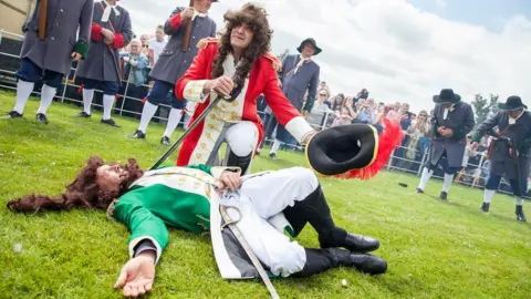 An actor playing King WIlliam III poses after defeating the actor playing King James II in the Sham Fight at Scarva