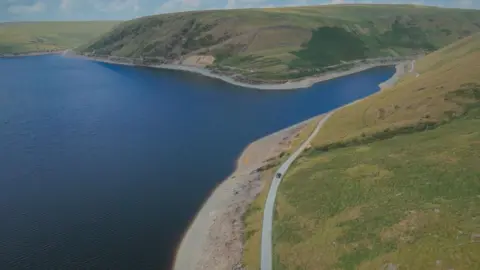 BBC Crimewatch An aerial view of a vast reservoir surrounded by rolling green hills and in the forefront of the image is a single car travelling on a winding country road.