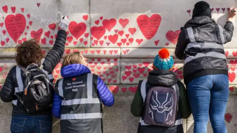 Getty Images Volunteers paint red hearts on the National Covid Memorial Wall in London in April 2021