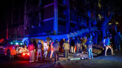 BBC/SHIRAAZ MOHAMED Residents of the derelict San Jose building in Johannesburg stand in line waiting to receive their share of bread, tinned food and a blanket from the Muslim Association of South Africa