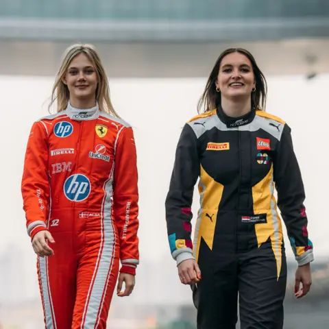F1 ACADEMY LTD/PARC FERMÉ Two female F1 Academy drivers pose for a photo on a race track 
